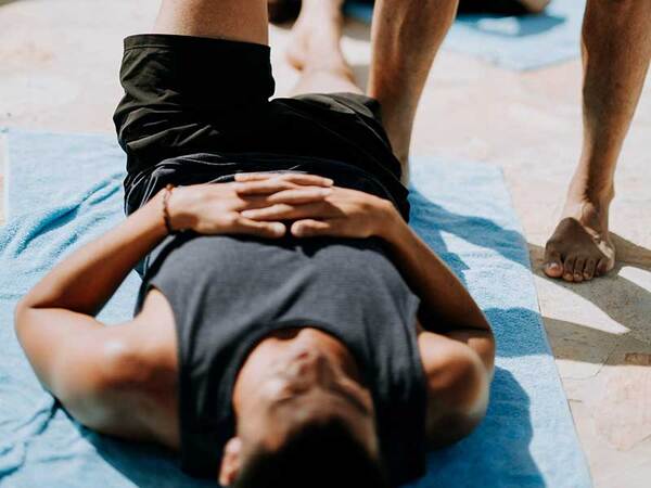 Felnőtt ember nyújt reggel egy napfényes nappaliban, jógamatracon ülve